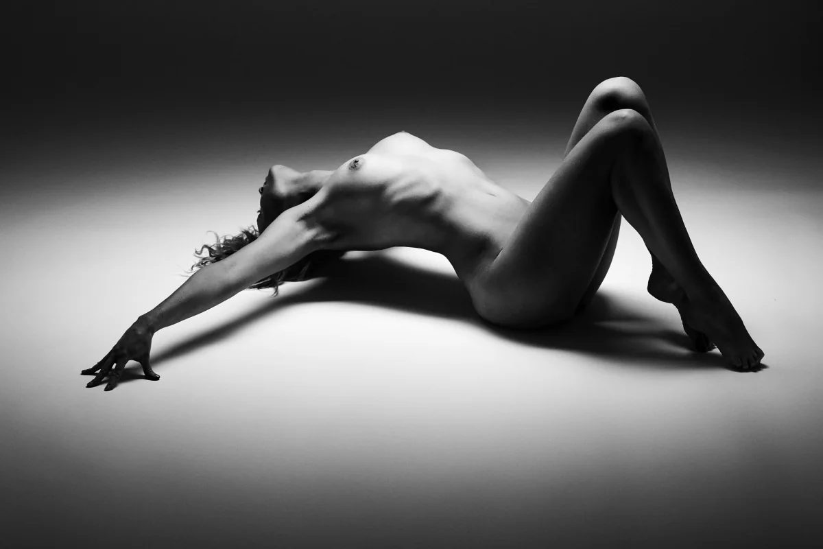 Pose de nu artistique en studio, éclairage sculptant la silhouette en noir et blanc